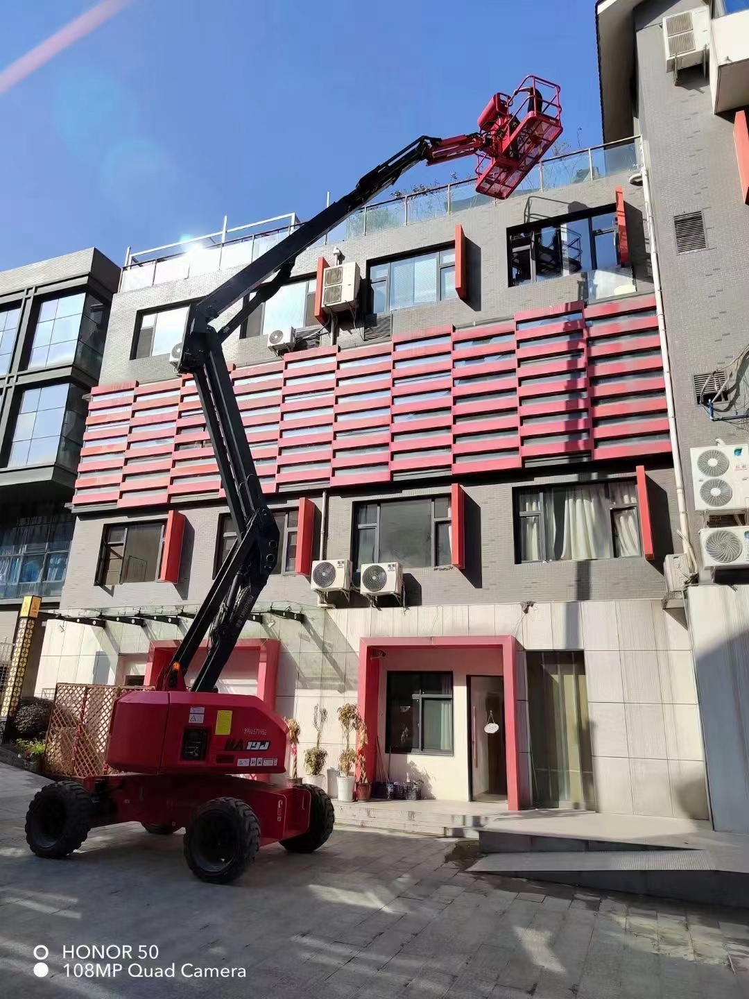 Red HERED HA19JE articulating boom lift in stowed position outside a factory