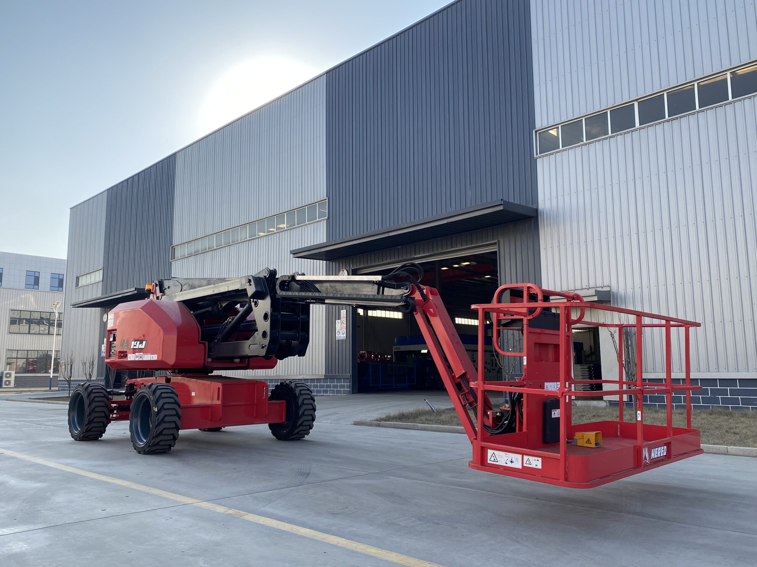 Red HERED HA19JE articulating boom lift in stowed position outside a factory