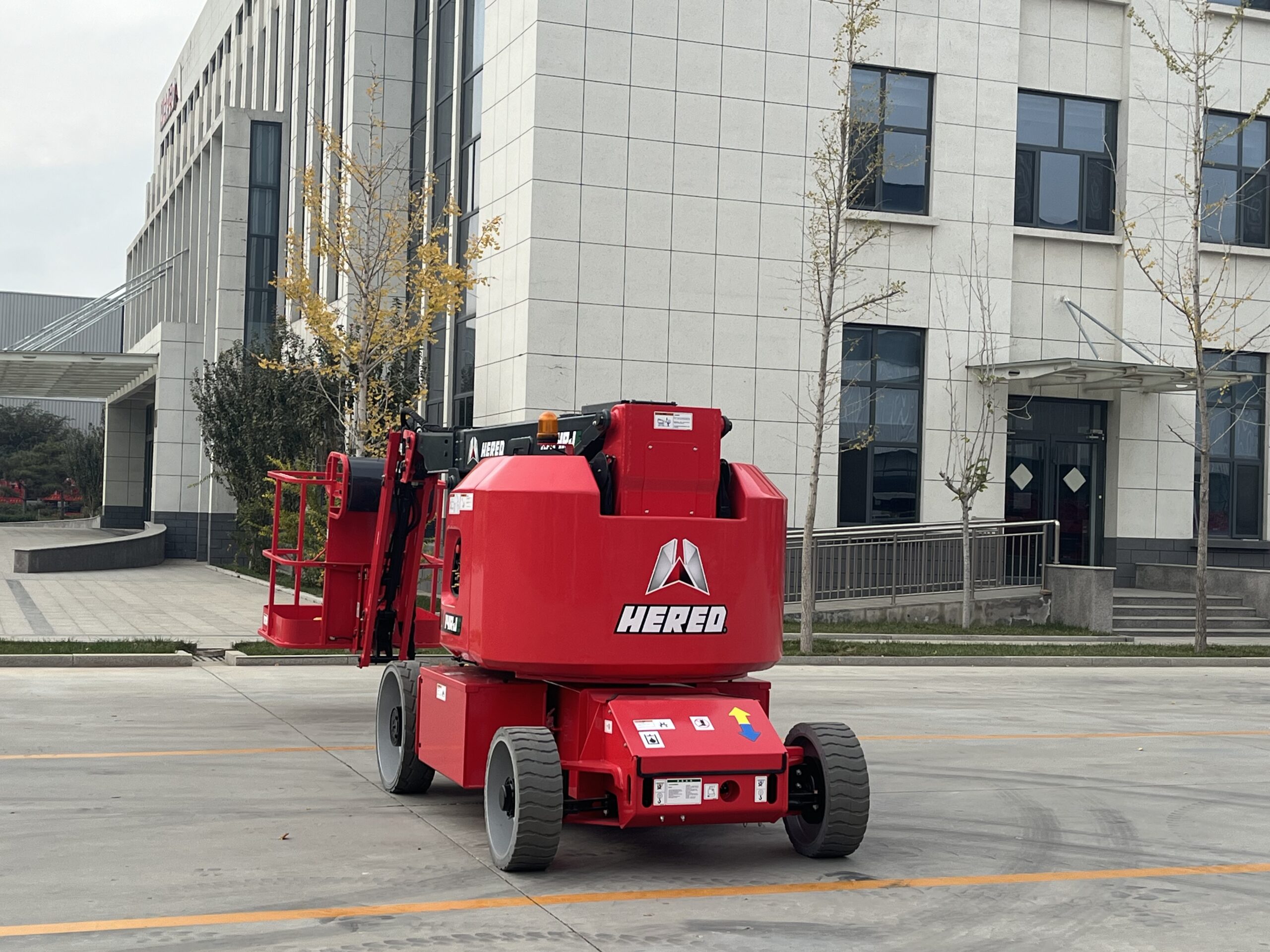 Red HERED HA14RJE articulating boom lift in stowed position, rear view