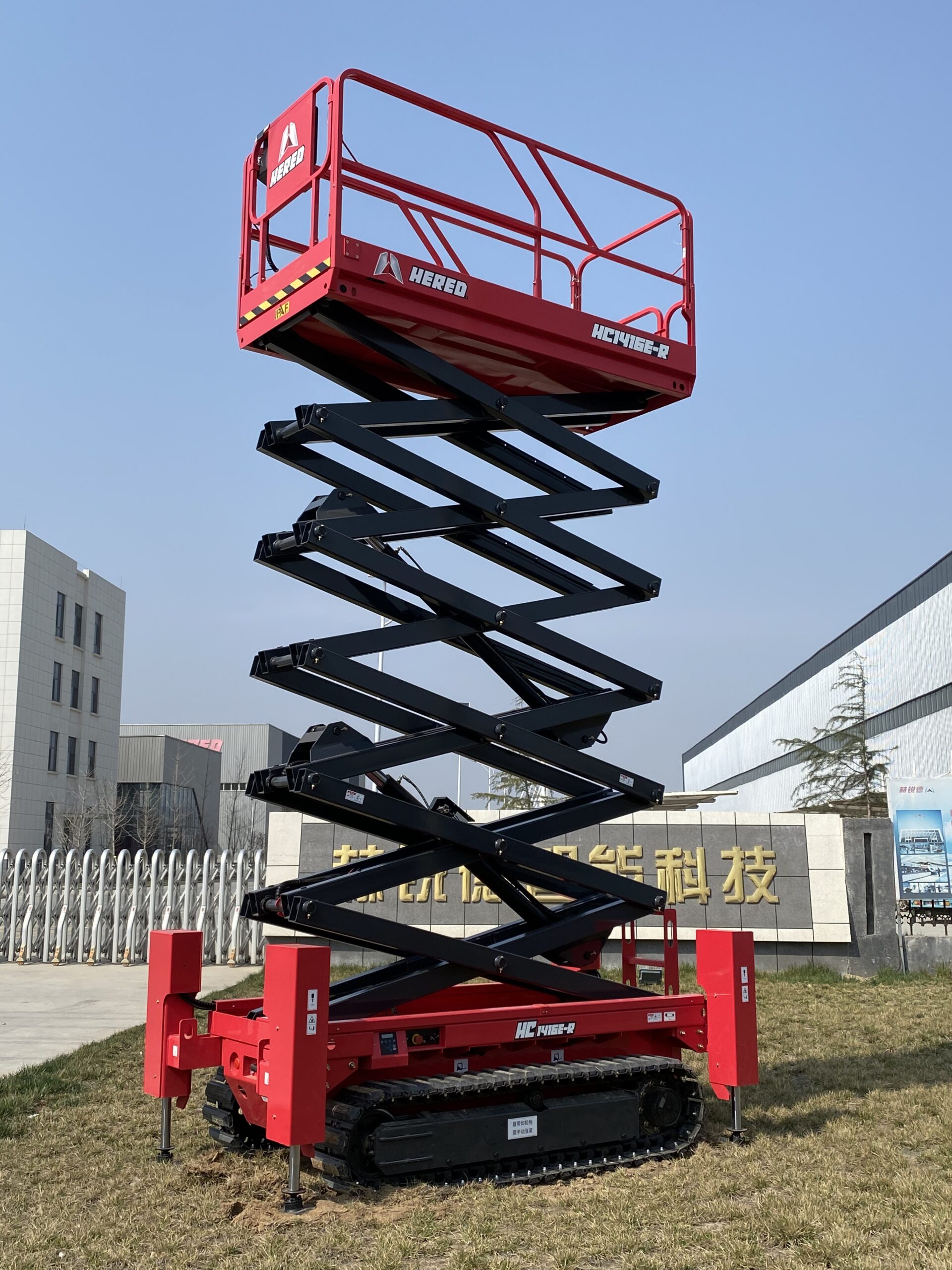 Red HERED HC1416ER crawler scissor lift in stowed position on grass