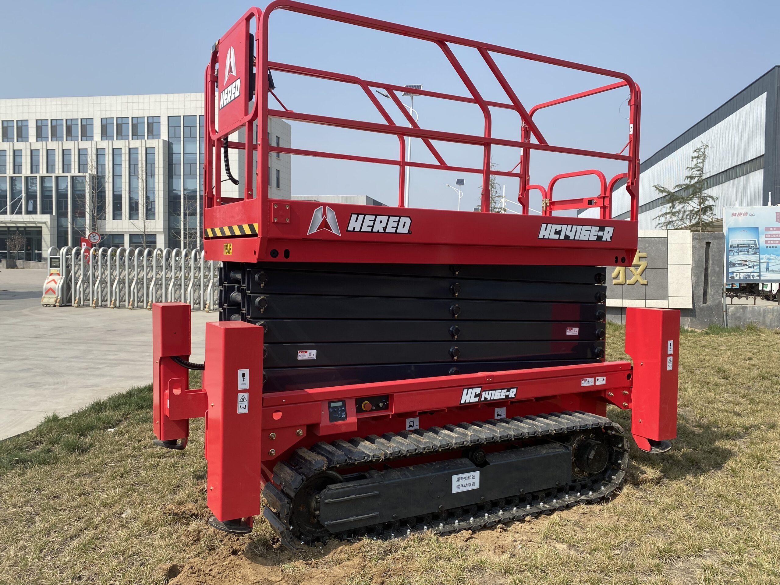 Red HERED HC1416ER crawler scissor lift in stowed position on grass